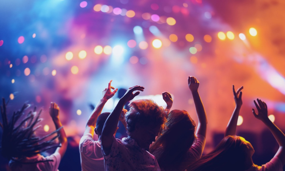 Crowd cheering at a concert with hands in the air and different color lights